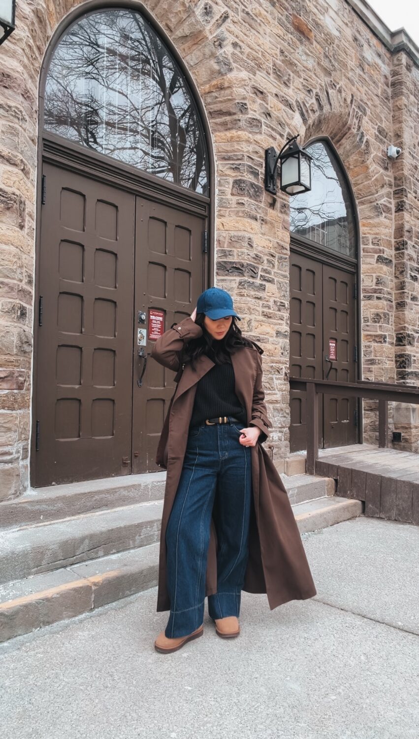 Quiet luxury street style outfit with trench coat and dark denim with cap and belt.